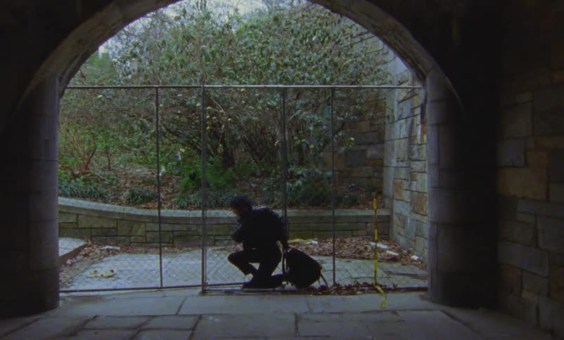 Person squeezes through closed gate at entrance of tunnel near hill
