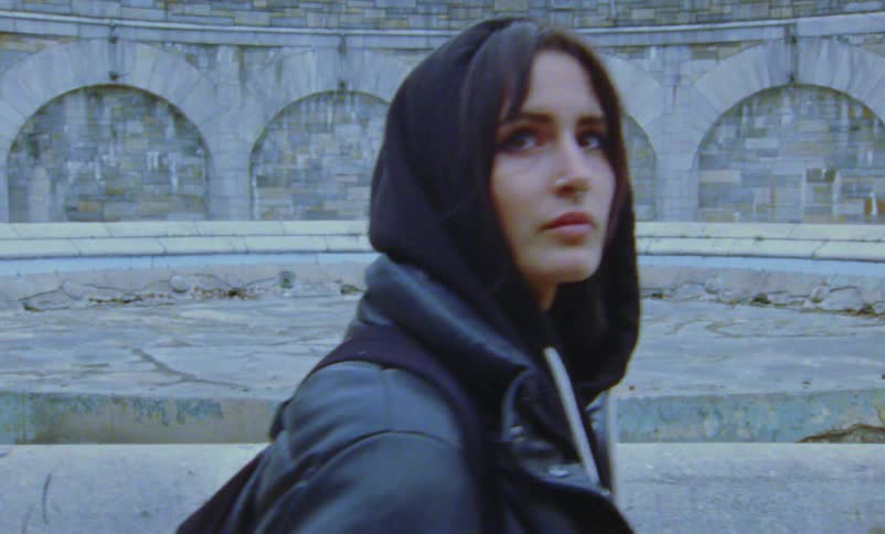 A woman is walking through a park and wearing a jacket