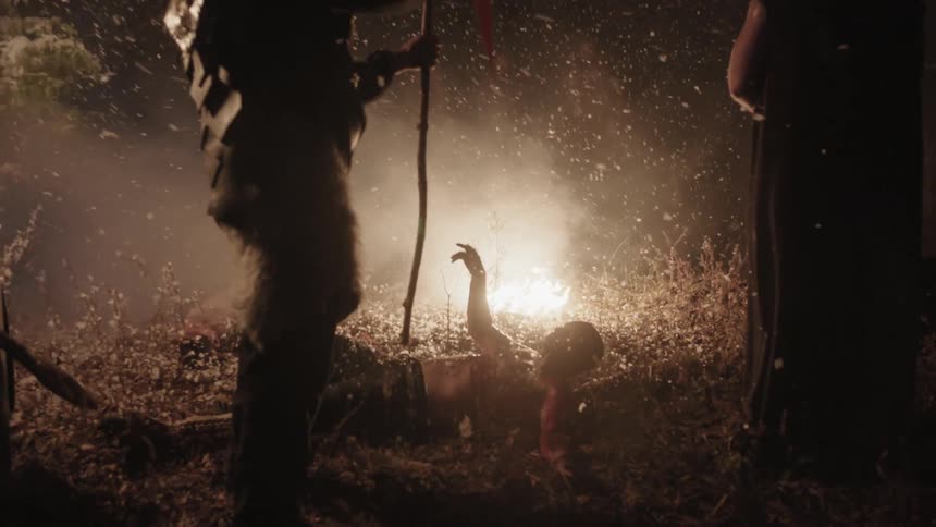 People stand around an injured man on the ground and one stabs a flag into him
