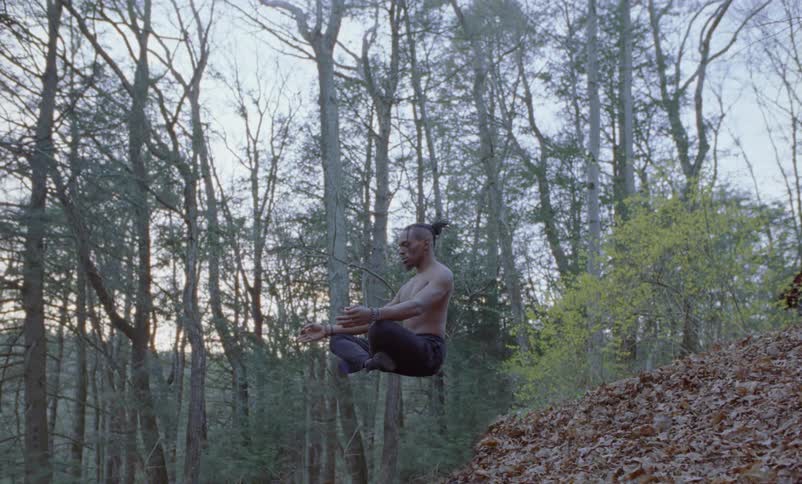 A man meditating with legs crossed floating above the ground levitating near trees