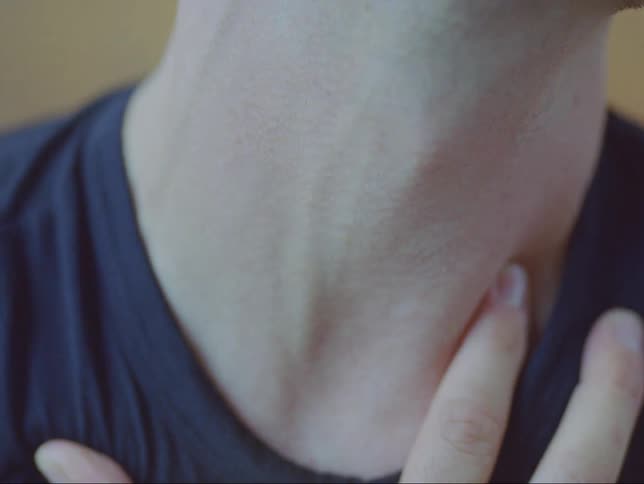 Close up of the neck of a man with a hand over his chest while swallowing
