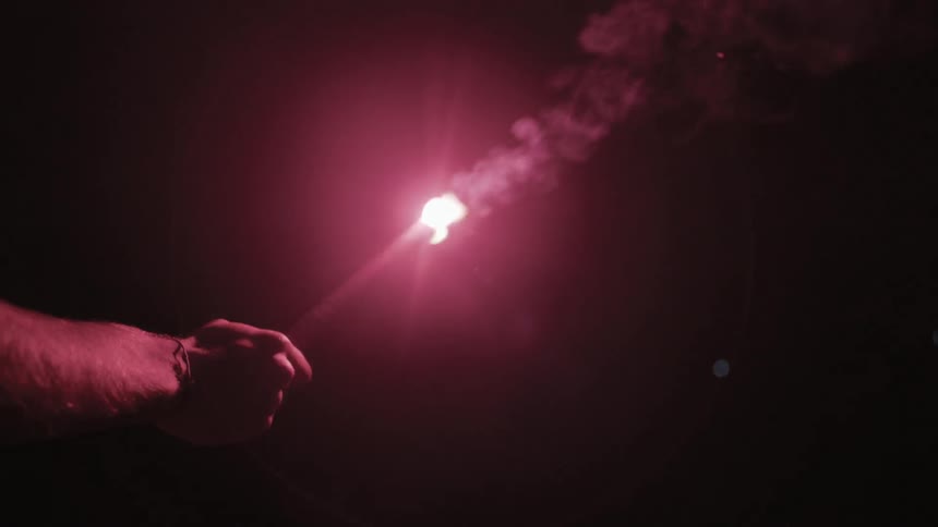 A male arm holds out a flare in a dark area