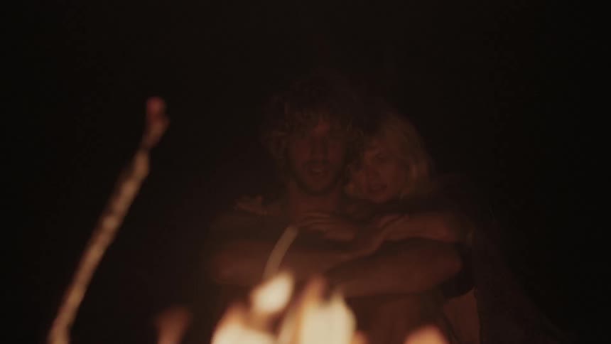 Man and woman sitting and embracing near a fire at night