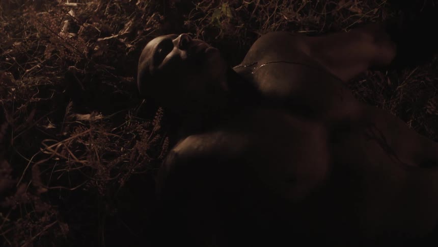 A large man laying on hay near a flickering fire