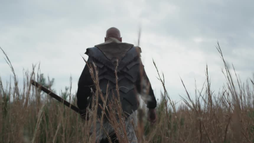 A large explorer walks through high grass holding an axe