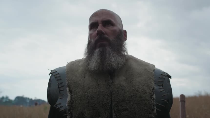 A large bearded explorer stands on an overcast day