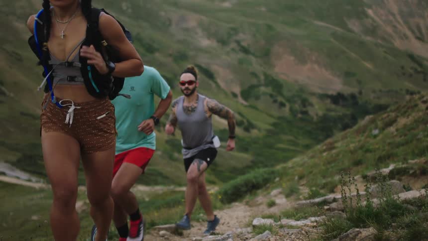 Three runners run up trail on slope of mountain