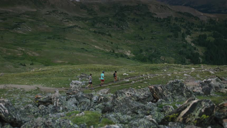 Three people run on a trail through a canyon