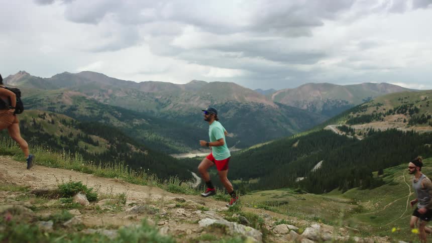Three runners sprinting up a mountainside on a cloudy day