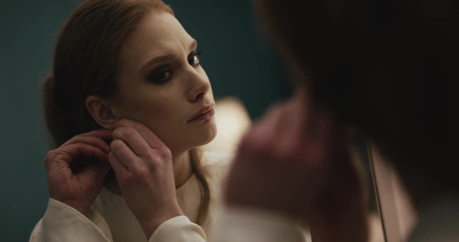 Sad woman with earrings makeup and brown hair looks in the mirror