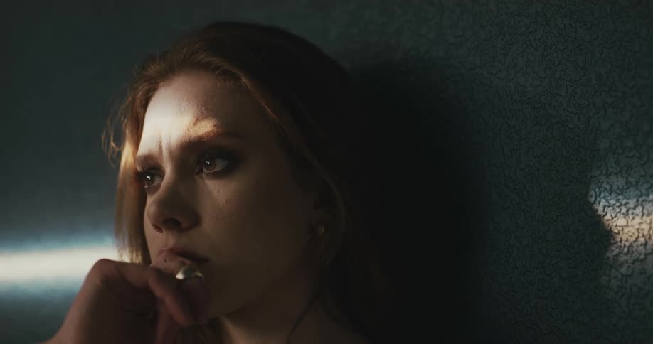 A nervous looking teenage girl leans against a wall and puts her hand up against her mouth
