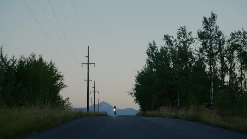 A cyclist pedals down a rural road as the sun sets