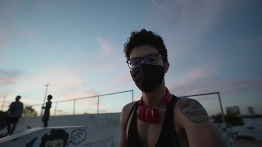 Man with glasses black mask red headphones black undershirt and skull tattoo takes selfie in skatepark at dusk