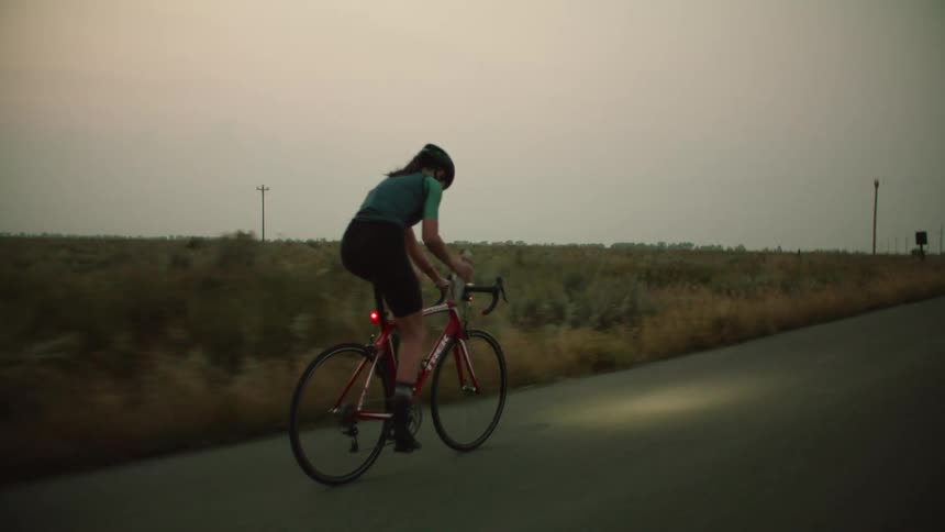 A cyclist takes a swig of water while riding her bicycle
