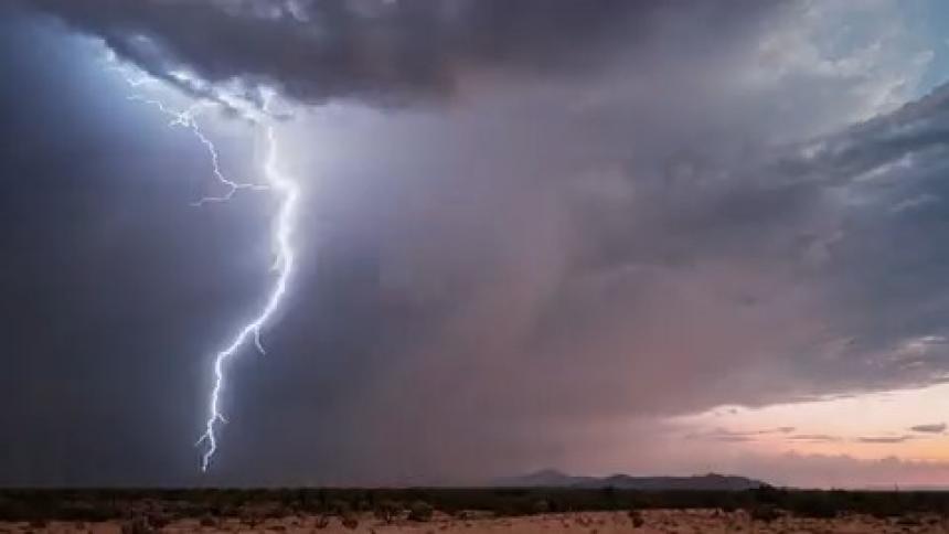 Dark storm clouds are overhead and a huge lightning bolt comes down and lights up the sky