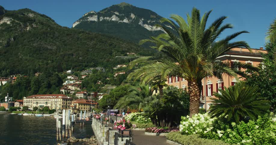 Two forest covered mountains tower over town and boats floating on water nearby