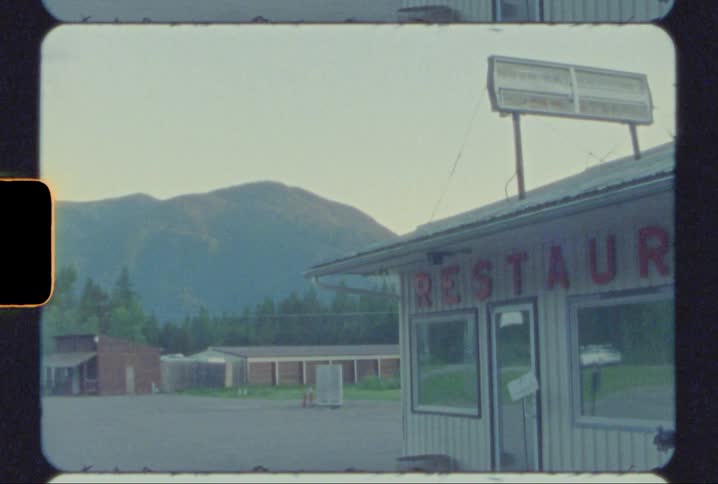 Vintage footage of cars driving past a restaurant in a small town shot on super 8mm film