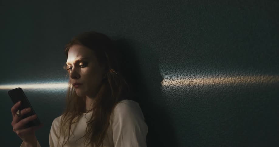 A woman is leaning against a wall and looking at her phone