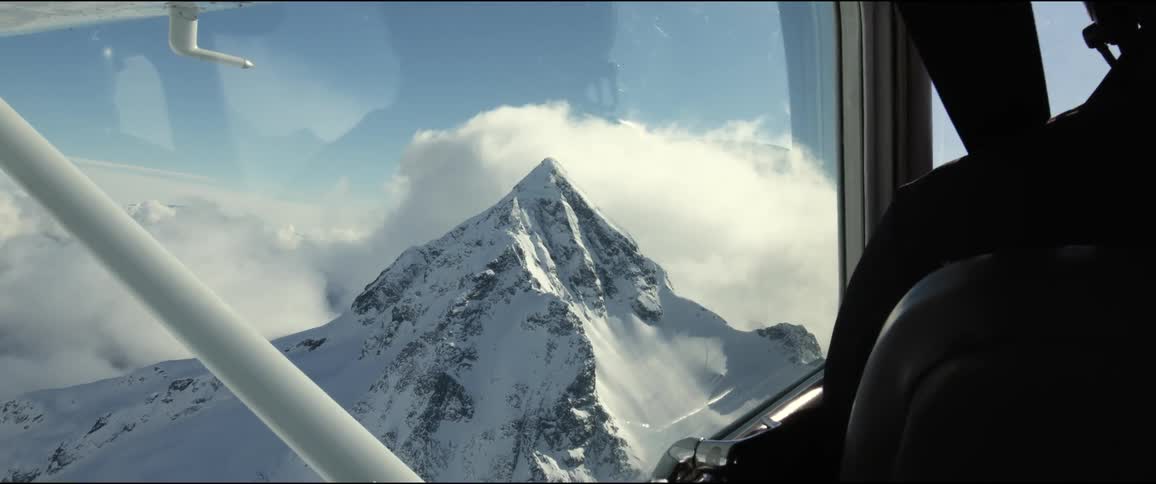 Pilot flies plane over snow covered mountain peak