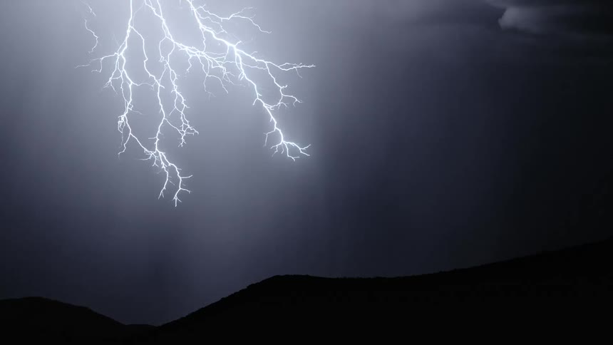 Lightning bolts crack the darkness of the night sky flashing as they spread over the mountains
