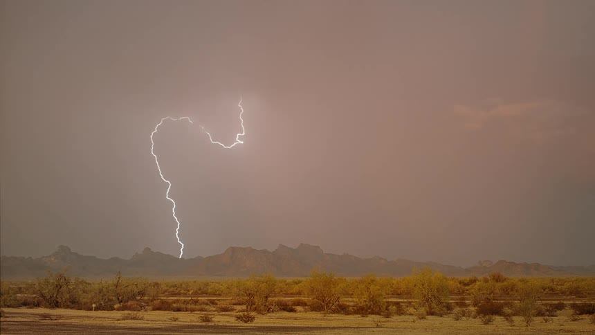 Lightning cracks and strikes over mountains and flashes in the clouds above