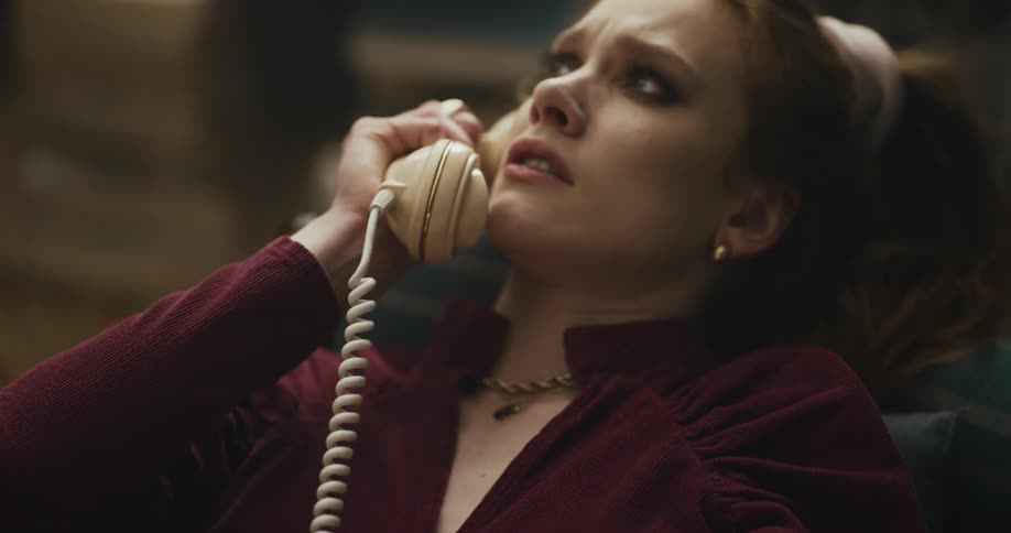 A woman is talking on a rotary phone and she has an upset look on her face as she pulls the receiver away from her ear