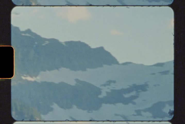 The peaks and slopes of a mountain range covered in snow in Glacier national park shot on 8mm film