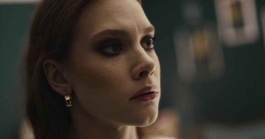 Woman wearing makeup stares to the side then at her reflection in a mirror before leaving