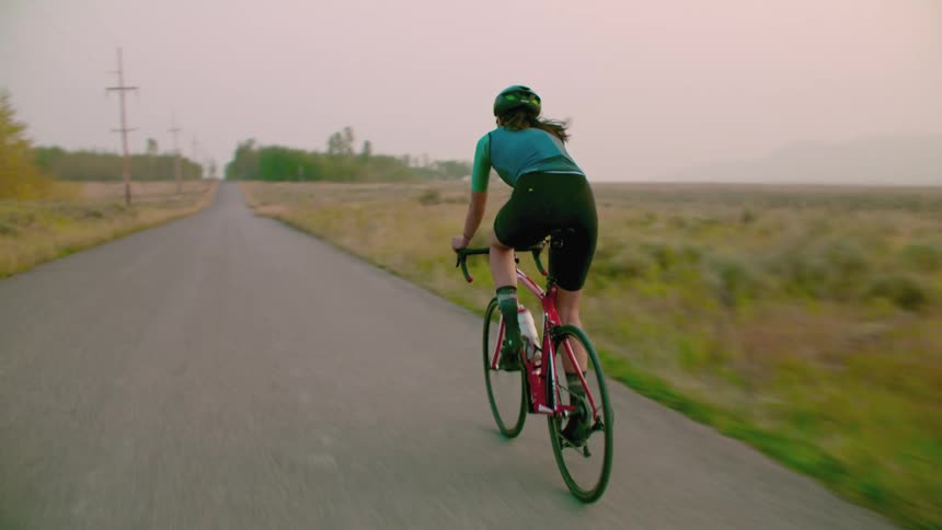 A woman is riding a bicycle on a rural road surrounded by trees in fall colors