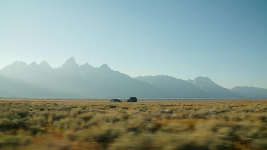 Two houses are out in the middle of open farmland and there are mountains in the distance in a hazy sky