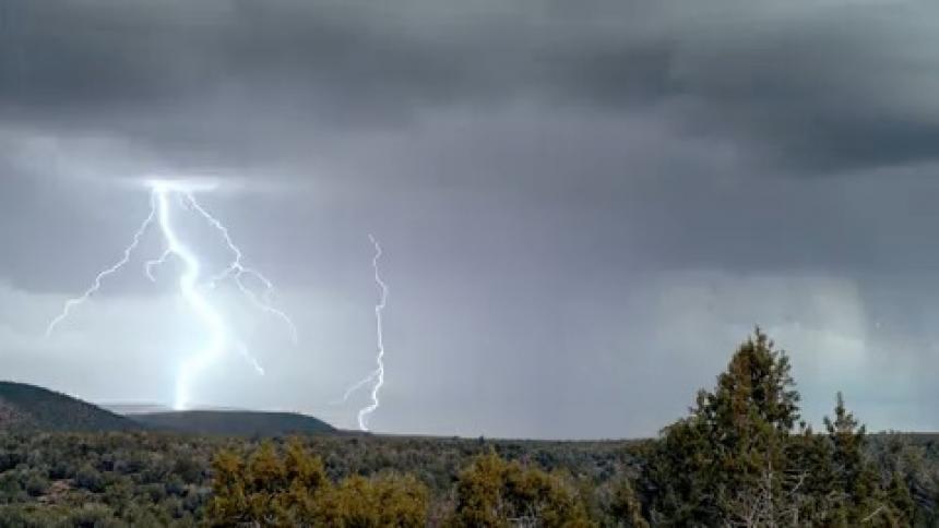 Lightning strikes and rain above a tree covered ridge