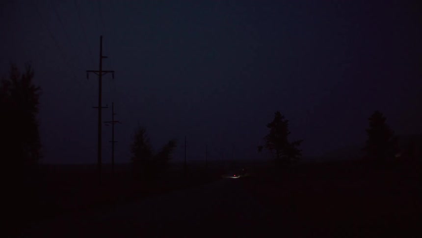 Dim light of a vehicle moving on a rural dirt road in the countryside at night