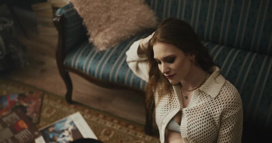 A woman is sitting on the floor leaning against a couch and shaking her head as it rests on her hand and she picks up a vinyl record album