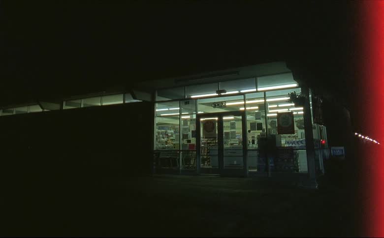 An empty store with red light glowing and reflecting on the glass at night shot on 16mm film