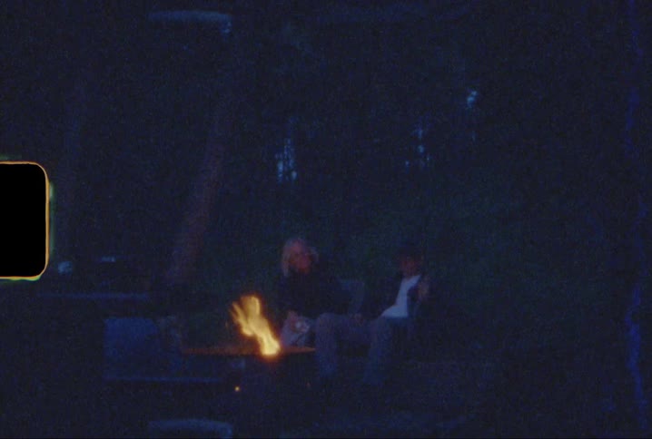 Two people sit by the campfire at night shot on super 8mm film
