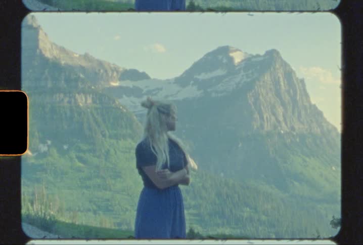 Girl stands outside with view of glacier national park behind her shot on 8mm film