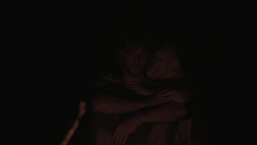 A man and woman cuddle near a fire at night