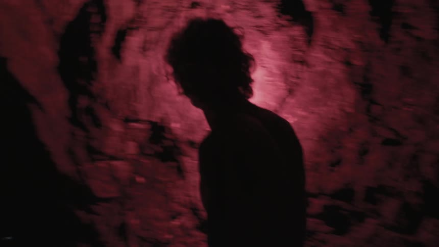 A man holds a flare up to a cave wall as he walks by it