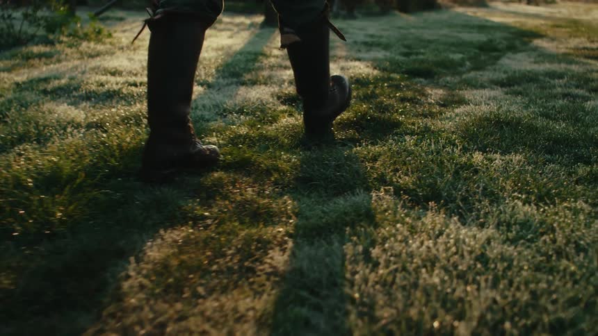 A person in boots walks through a field during the day