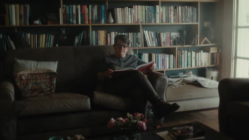 A woman sitting on a sofa and reading a book in a home library