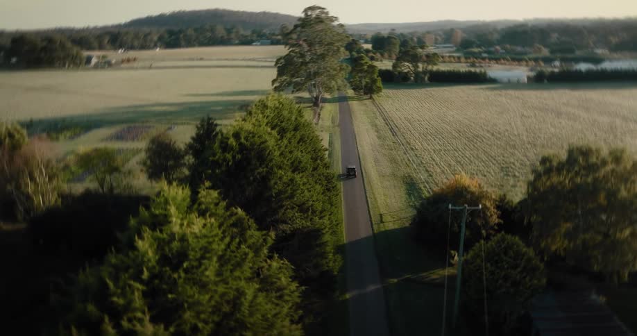 Aerial view of a car driving on a country road surrounded by farming fields