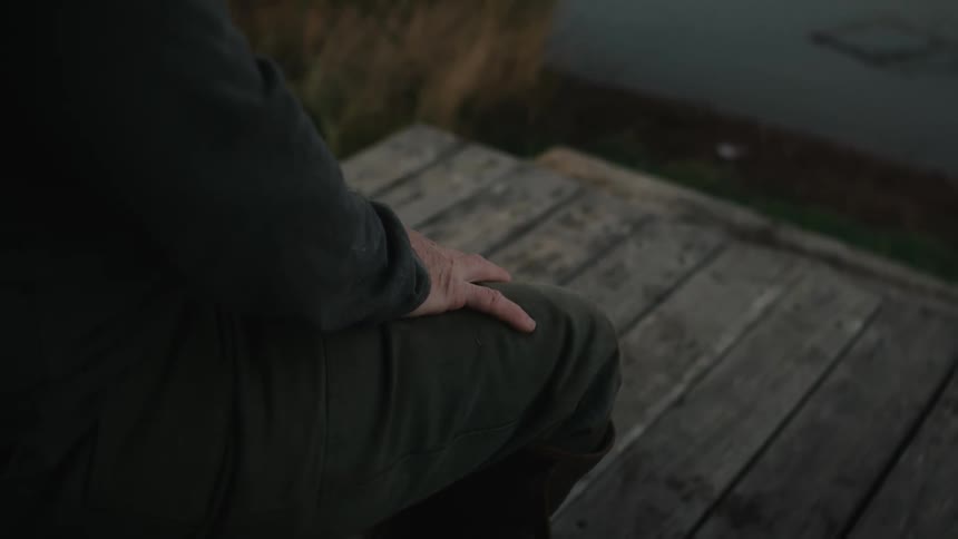 A person sitting on a wooden deck steps away from a pond