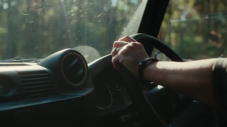 A woman is holding the steering wheel as she drives an automobile through the woods