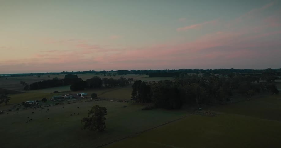 Green fields and trees with a farmhouse and buildings at sunrise