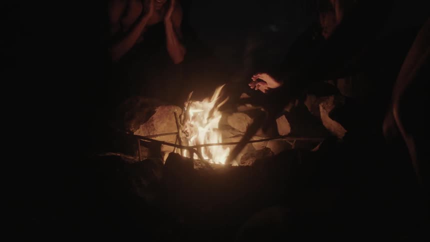 Several people warm their hands over a small fire