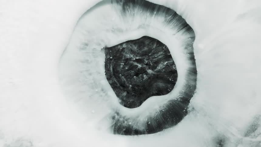 White floating ink shaped like an iris erupting and contracting over a dark background