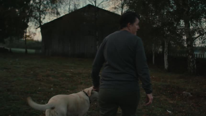 Farmer walks with her dog through a fence into the fields at morning