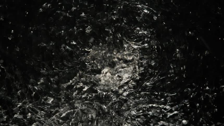 A shiny substance ripples and moves in the darkness as light reflects on the edges