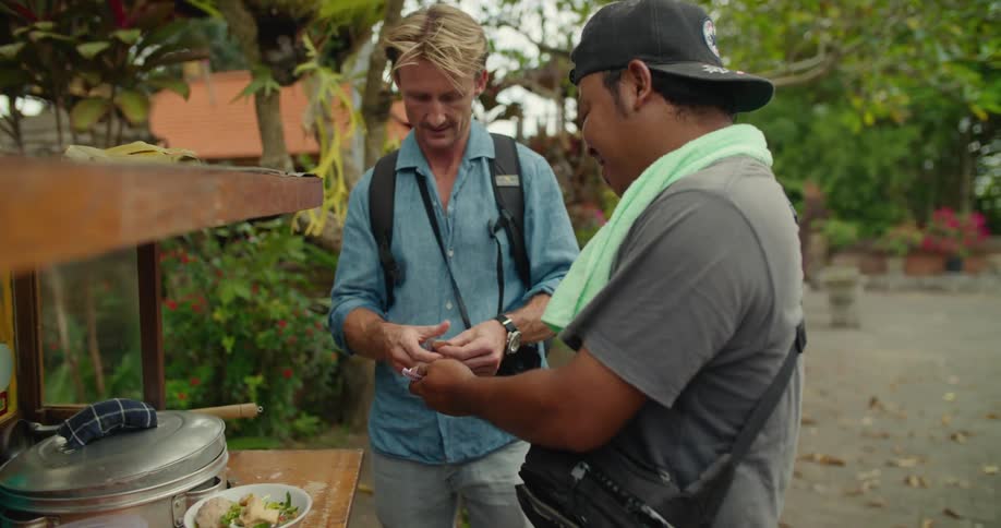 A tourist pays a food cart vendor with paper money as they chat
