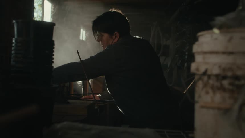 Man picks up various tools from a dusty dimly lit shed in the morning